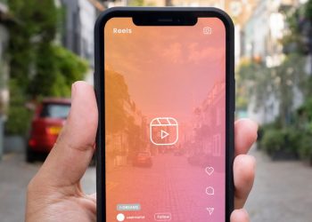 Homem segura celular ligado na câmera com filtro rosa mostrando a rua - melhores plataformas para ganhar visualizações reels