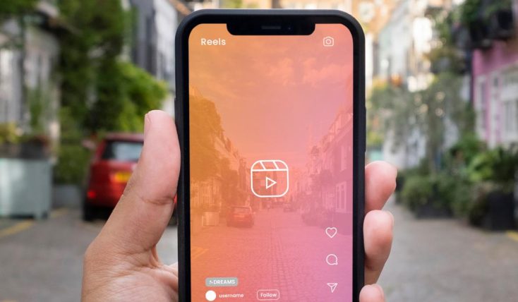 Homem segura celular ligado na câmera com filtro rosa mostrando a rua - melhores plataformas para ganhar visualizações reels